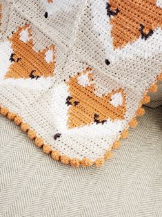 an orange and white crocheted blanket with foxes on it