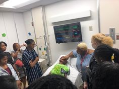 a group of people standing around a woman in a hospital bed looking at something on the monitor screen