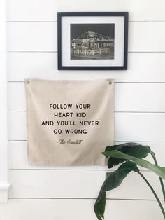 a black and white photo hanging on the wall next to a plant with a quote