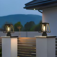 two lamps sitting on top of a white fence next to a building with mountains in the background