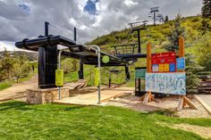 a sign in front of a ski lift on the side of a hill with grass and trees