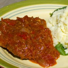 a green and white plate topped with meat covered in sauce next to mashed potatoes