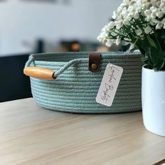 a green basket with a wooden handle on a table next to a white vase filled with flowers