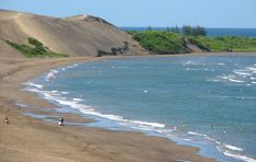 people are walking along the beach by the water