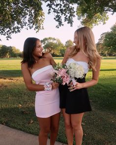 two beautiful young women standing next to each other in front of a tree and grass field