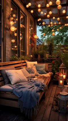 a porch covered in lots of lights next to a wooden bench with pillows and blankets on it