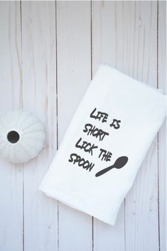 a kitchen towel with the words life is short look the spoon on it next to a ball of yarn