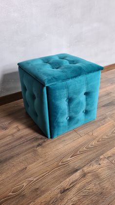 a blue ottoman sitting on top of a hard wood floor next to a white wall