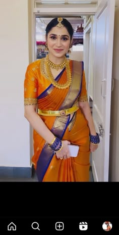 a woman in an orange and blue sari with gold jewelry on her neck, standing next to a door