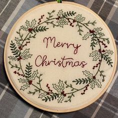 a cross stitch christmas ornament hanging on a plaid tablecloth with the words merry christmas