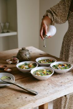 a woman is pouring some soup into her bowls on the table with spoons and utensils