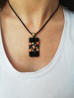 Bronze-colored rectangular pendant necklace. This mosaic jewel is embellished with ceramic and black and orange millefiori. The pendant is covered with epoxy resin providing shine. This necklace attaches with a black waxed cotton link, finished with a bronze carabiner clip which will allow you to put it on easily. This piece of jewelry will bring a touch of originality to your everyday outfits. Unique and original piece. Rectangle Pendant Necklace, Outfits Unique, Ceramic Mosaic, Bronze Frame, Rectangle Pendant, Carabiner Clip, Black And Orange, Waxed Cotton, Bronze Color