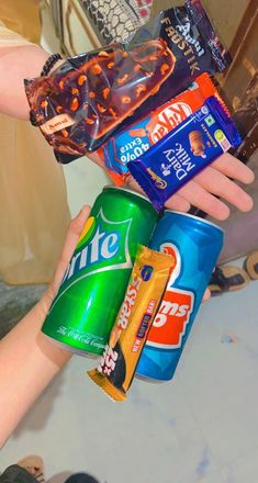 a person holding several different types of snacks in their hands, including chips and soft drinks