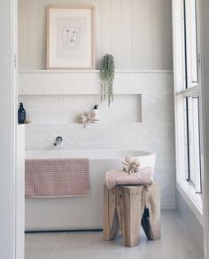 a bathroom with a white tub and wooden stool next to the bathtub is decorated in neutral colors