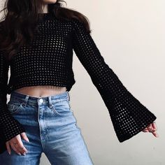 a woman with her arms outstretched wearing jeans and a cropped top is standing in front of a white wall