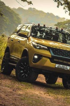 a yellow pick up truck parked on top of a dirt road in front of trees