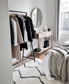 a bedroom with a bed, mirror and clothes on hangers in front of a window