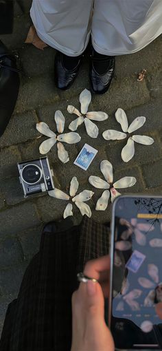 two people standing next to each other with cell phones and paper flowers on the ground