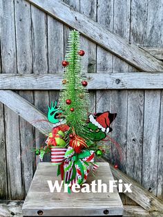 a small christmas tree sitting on top of a wooden table next to a fence with the words wheatfix above it