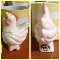 there are two ceramic chickens on the table next to each other and one has a cup in front of it