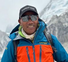 a man in an orange and blue jacket standing on top of a snow covered mountain