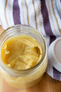 a jar filled with yellow liquid sitting on top of a wooden table next to a striped towel