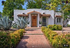 a white house with red brick walkway leading to the front door and entry way surrounded by greenery