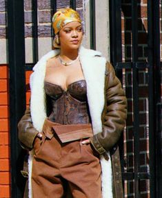 a woman standing in front of a gate wearing a brown outfit and fur collared coat