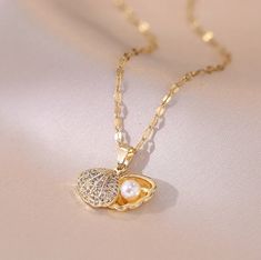 Let the magic of the ocean become a part of your jewelry collection with our enchanting Seashell Pendant Necklace. This stunning piece features a beautifully crafted golden clam shell, adorned with the tiniest crystal diamonds with a pearl nestled inside. The pendant has a unique, movable element allowing it to be opened or closed, revealing or concealing the pearl inside. This captivating feature makes the necklace not just a piece of jewelry, but a conversation starter and a treasured keepsake Necklace With Pearl, Seashell Pendants, Gold Chain With Pendant, Luxury Necklace, Shell Necklace, Hawaiian Style, Pearl Pendant Necklace, Luxury Style, Shell Necklaces