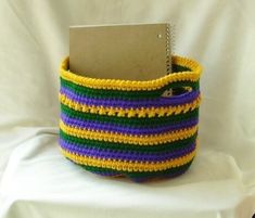 a colorful crocheted basket with a notepad in it on a white background