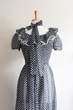 "Vintage 1960s/1970s maxi dress in black and white polka dot print sheer fabric with scoop neckline, fitted bodice, smocked detail along front bodice, overly ruffled trim along neckline, short puff sleeves, waist seam, matching sash belt that can be worn multiple ways, full gathered maxi length skirt, gathered ruffle panel along hem, and back zipper. Dress is quite sheer - best worn with slip if that is not desired look. Good vintage condition. full garment measurements: bust: 32\" - 35\" waist: Fitted Swiss Dot Dress With Square Neck, Fitted Swiss Dot Square Neck Dress, Fitted 1950s Polka Dot Dresses, 1950s Style Fitted Polka Dot Dresses, 1950s Style Summer Dress With Ruffles, 1950s Style Ruffled Summer Dress, Vintage Fitted Dress With Smocked Bodice, Fitted Retro Swiss Dot Dress, Retro Fitted Swiss Dot Dress