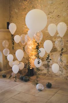 white balloons and greenery are on the floor in front of a stone wall with a fireplace