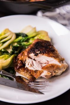 a white plate topped with meat and veggies next to a knife and fork