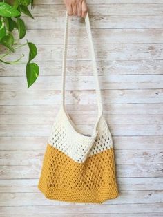 a woman holding a yellow and white crocheted bag next to a potted plant