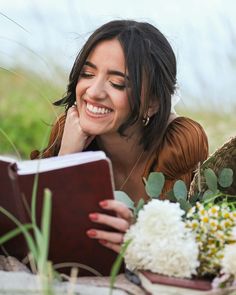 a woman laying down reading a book on the ground with flowers in front of her