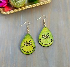 Elevate your holiday look with these Grinch tear drop earrings! Laser-cut wood makes for a lightweight feel, these whimsical earrings feature the iconic Grinch grin, hand-painted and sealed for a festive touch. Perfect for adding a dash of holiday spirit to any outfit, these earrings are a must-have accessory. Grab yours now and spread the joy with this playful and charming Grinch-inspired design! Earwires are hypoallergenic and lead and nickle free. Choose light gold color (pictured), antique gold color, or surgical stainless steel. Painted Christmas Earrings, Guy Earrings, Grinch Earrings, Whimsical Earrings, Wood Jewelry Diy, Light Gold Color, Tear Drop Earrings, Earring Ideas