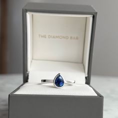 a white gold ring with a blue diamond in it's presentation box on a table