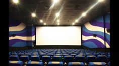 an empty movie theater with blue chairs and white screen in front of the projector