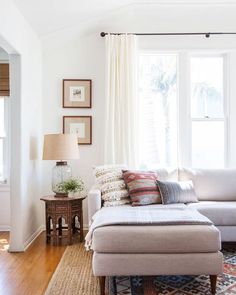 a living room with a couch, ottoman and rug in front of a large window