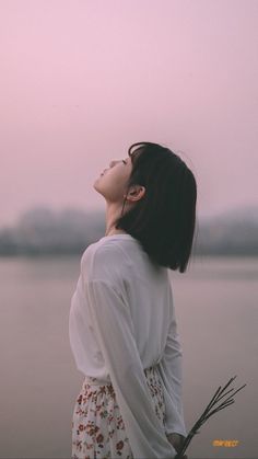 a woman standing next to a body of water with her eyes closed and looking up at the sky