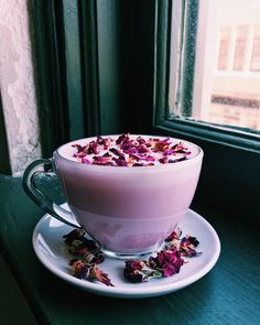 a cup filled with pink liquid sitting on top of a saucer next to a window