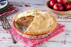 an apple pie on a plate with a bowl of apples in the background