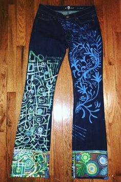 a pair of jeans with different designs on them sitting on top of a wooden floor