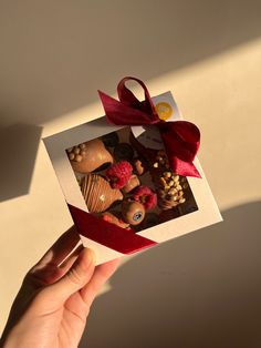 a hand holding up a box of chocolates with a red bow on it's ribbon