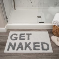 a bathroom rug that says get naked on the floor next to a basket with towels