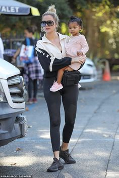 a woman holding a baby in her arms while walking down the street with other people