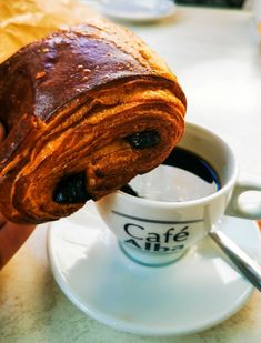 a croissant is being dipped with blueberries in a white cup on a saucer