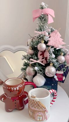 a small christmas tree with ornaments on it and two mugs sitting next to it