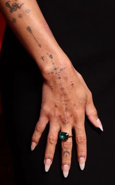 a woman's hand with tattoos on it and a green stone in the middle