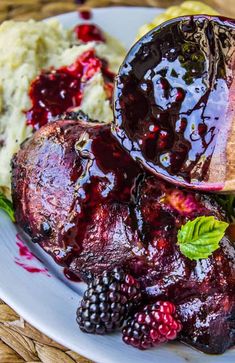 a white plate topped with meat covered in blackberry sauce next to mashed potatoes and berries